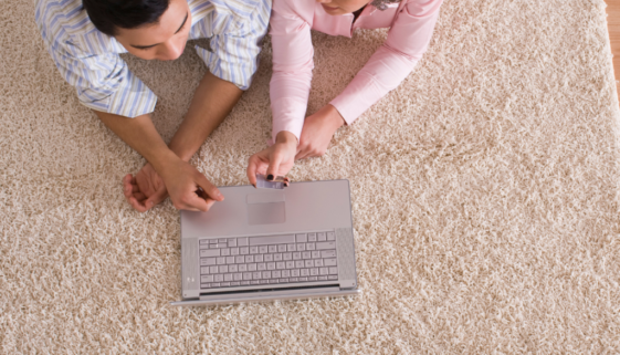 young couple laying down on a rug and working on a laptop