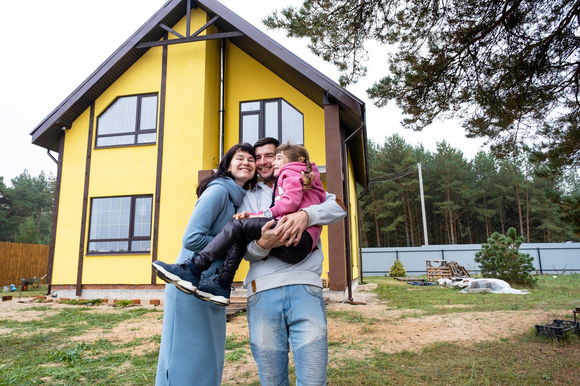 Happy family in the yard of an unfinished house - purchase of a cottage